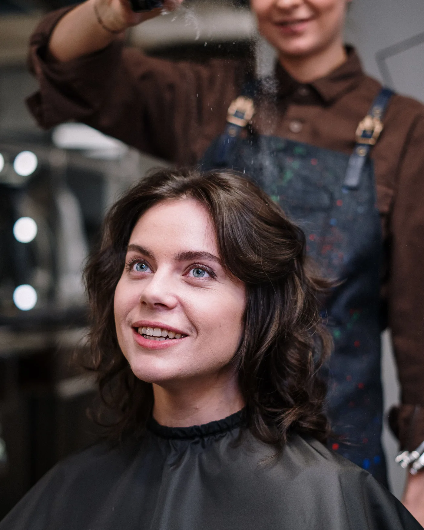 Profissional de beleza sorrindo enquanto conversa com uma cliente na cadeira